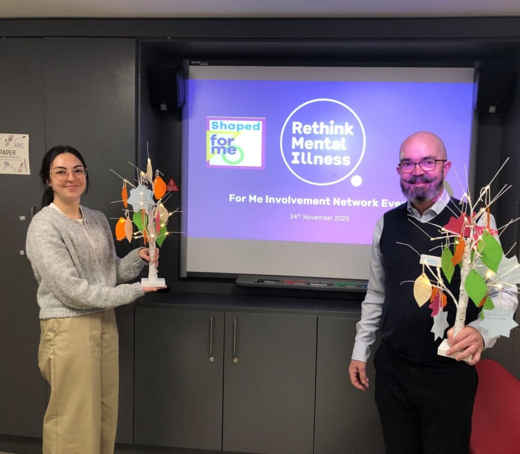 Team members standing with trees of hope in front of screen with Rethink Mental Illness at the event